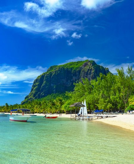boats on sea shore near green mountain under blue sky during daytime