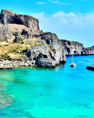 white boat on blue sea near brown rocky mountain under blue sky during daytime
