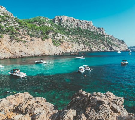 white and blue boat on sea near green mountain during daytime